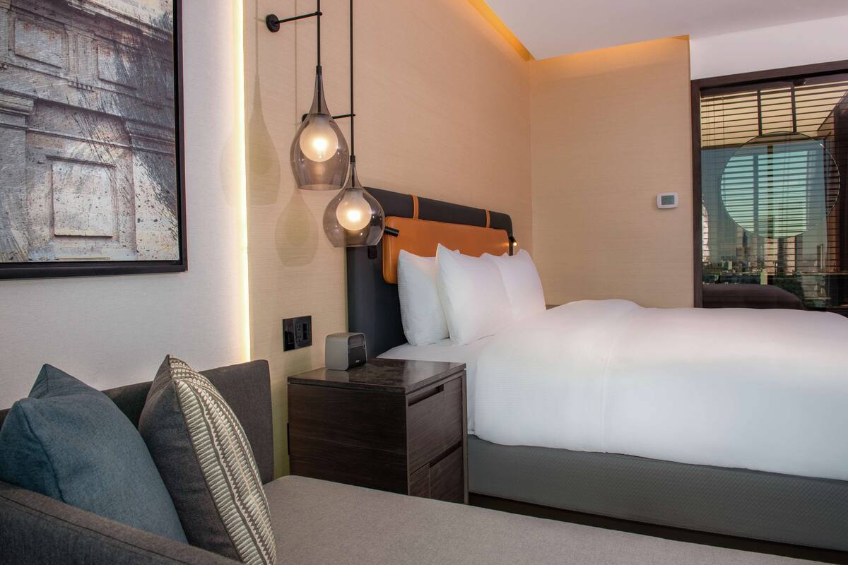 Een moderne hotelkamer met een groot bed, een nachtkastje met lamp, een sofa en een kunstwerk aan de muur.