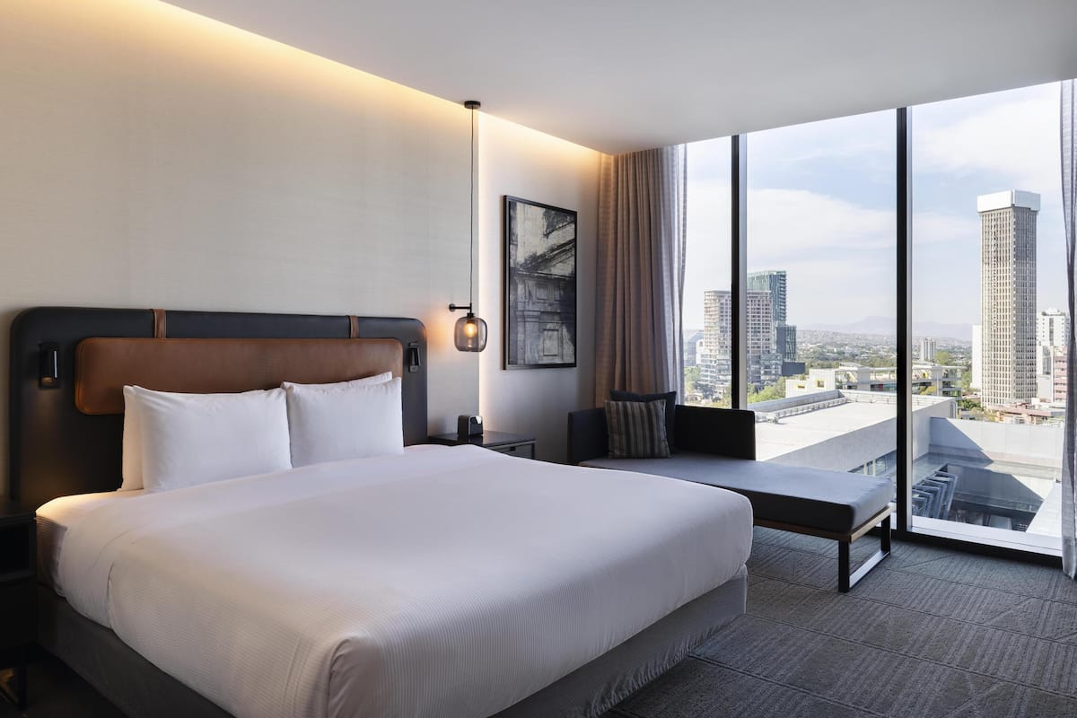 Een hotelkamer met een groot bed, een bureau en uitzicht op hoge gebouwen.