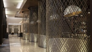 Een moderne hotellobby met een spiegelende vloer, een zithoek met stoelen en een grote, verlichte bolvormige lamp.