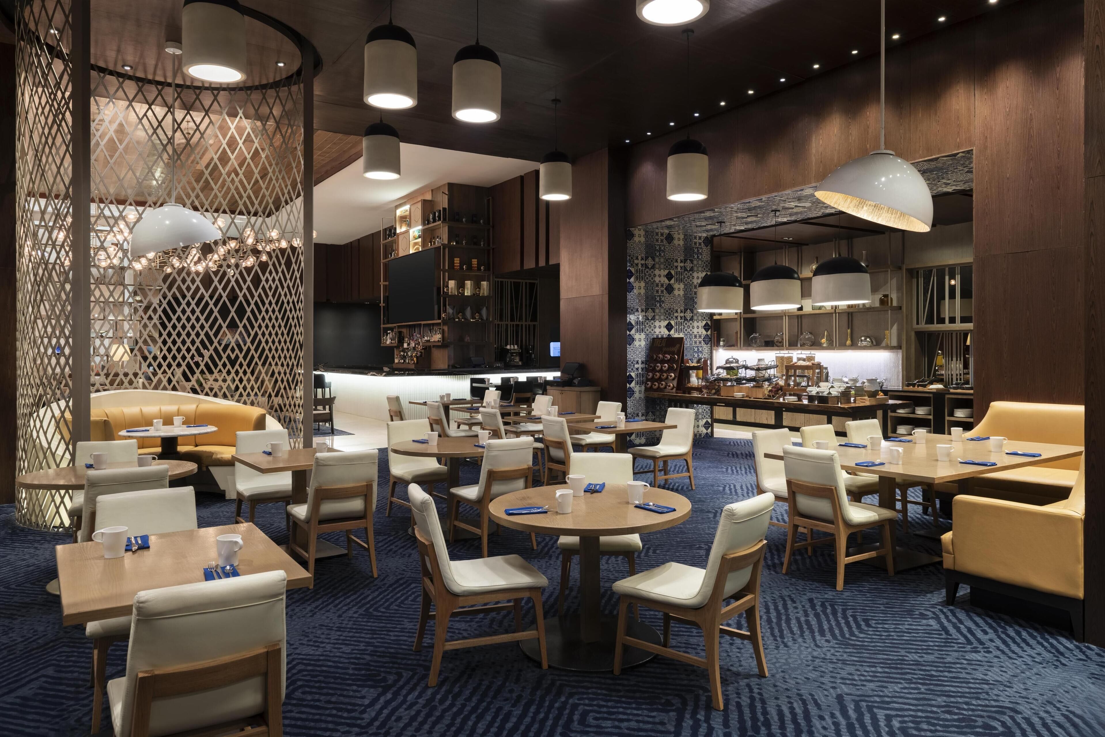 A modern hotel lobby with round tables, chairs, a bar area, and a seating area with a sofa.