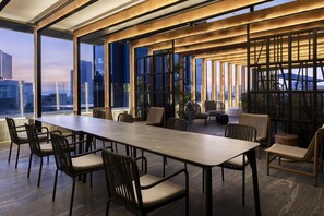 A modern conference room with a long table and chairs, large windows with city views, and a wooden ceiling structure.