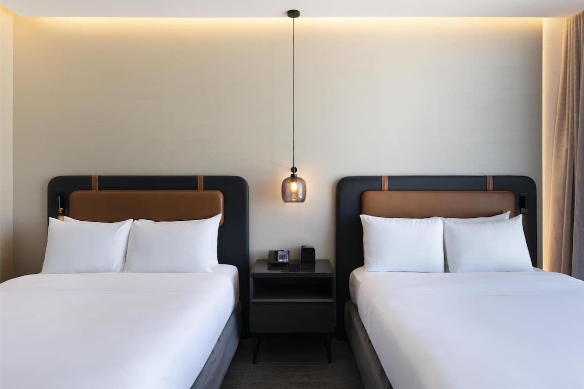 Een hotelkamer met twee bedden, een nachtkastje met lamp en een wandlamp.