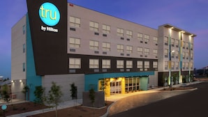 A hotel with a modern design, featuring a prominent 'tru by Hilton' sign, multiple windows, and a well-lit entrance.