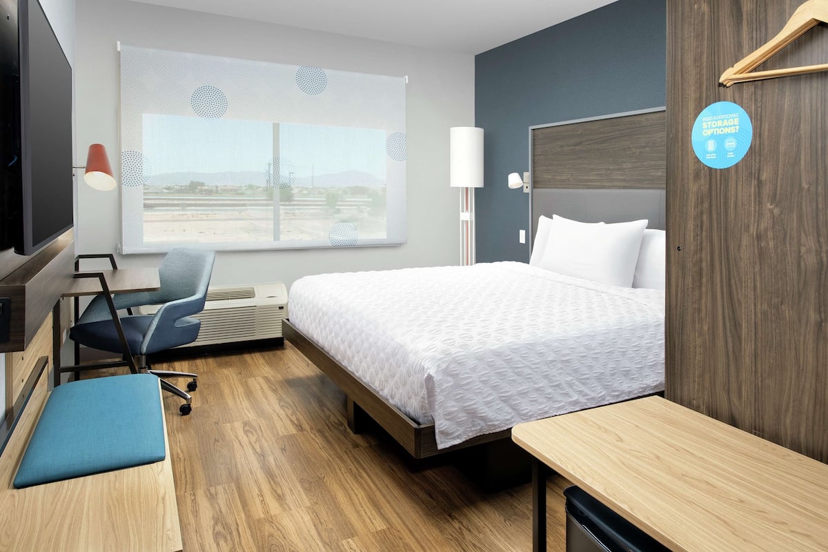 Une chambre d’hôtel équipée d’un lit, d’un bureau, d’une chaise, d’une télévision et d’une fenêtre donnant sur un paysage agréable.