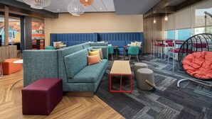 A modern lounge area with a blue cushioned sofa, red and orange ottomans, a wooden coffee table, and a hanging chair with a red cushion.