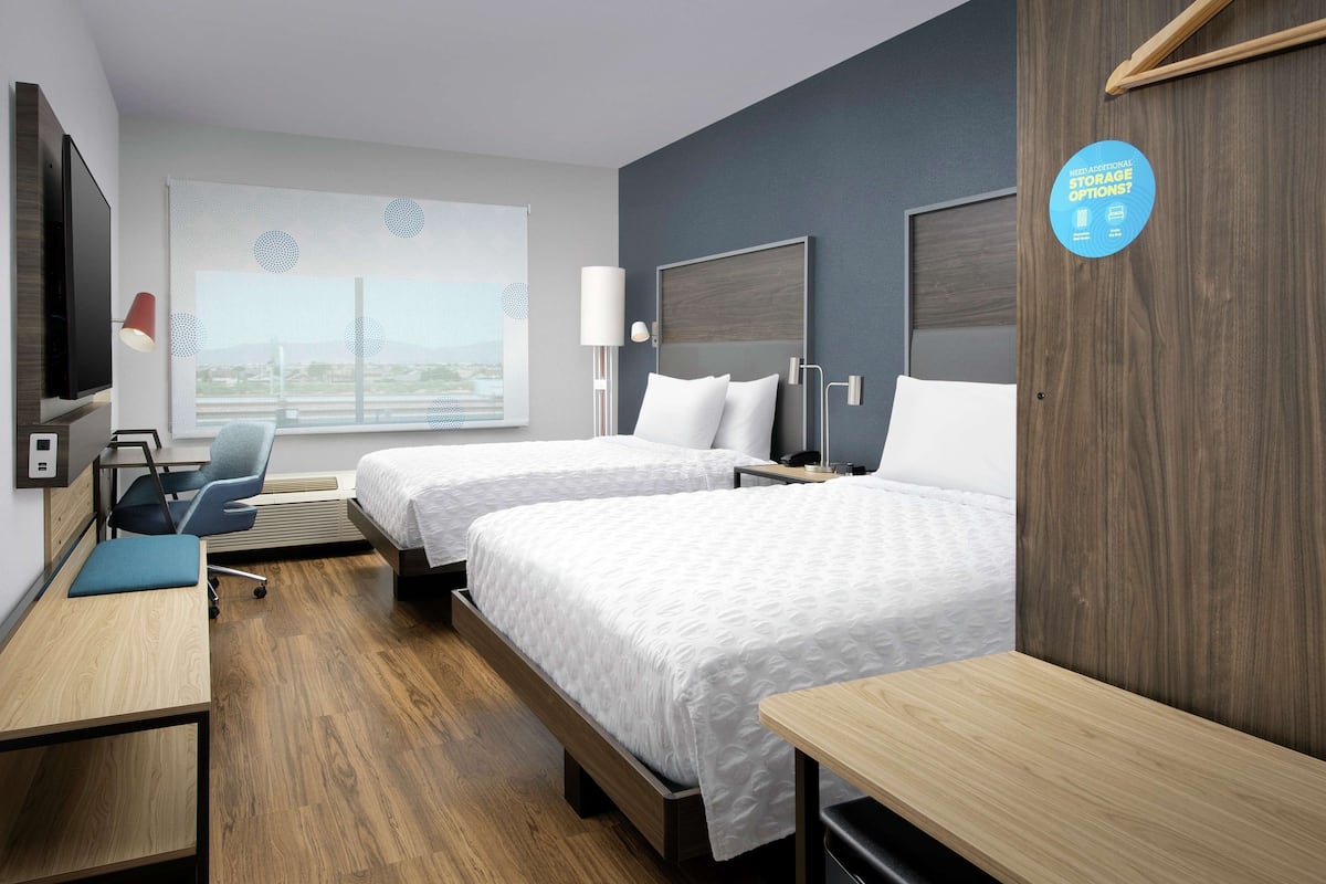 Une chambre d’hôtel avec deux lits, un bureau, une chaise, une télévision et une fenêtre donnant sur un beau paysage.