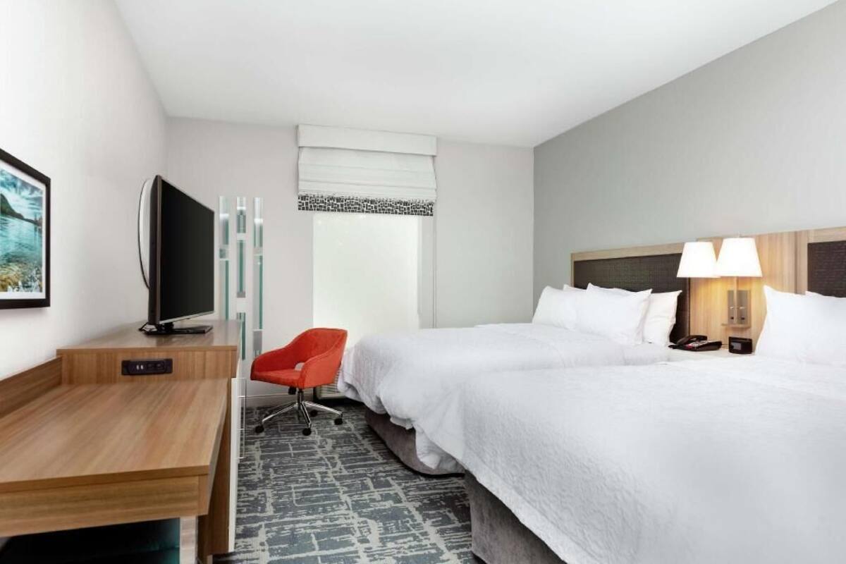 A hotel room with a bed, a desk, a TV, a chair, and a window with a view.
