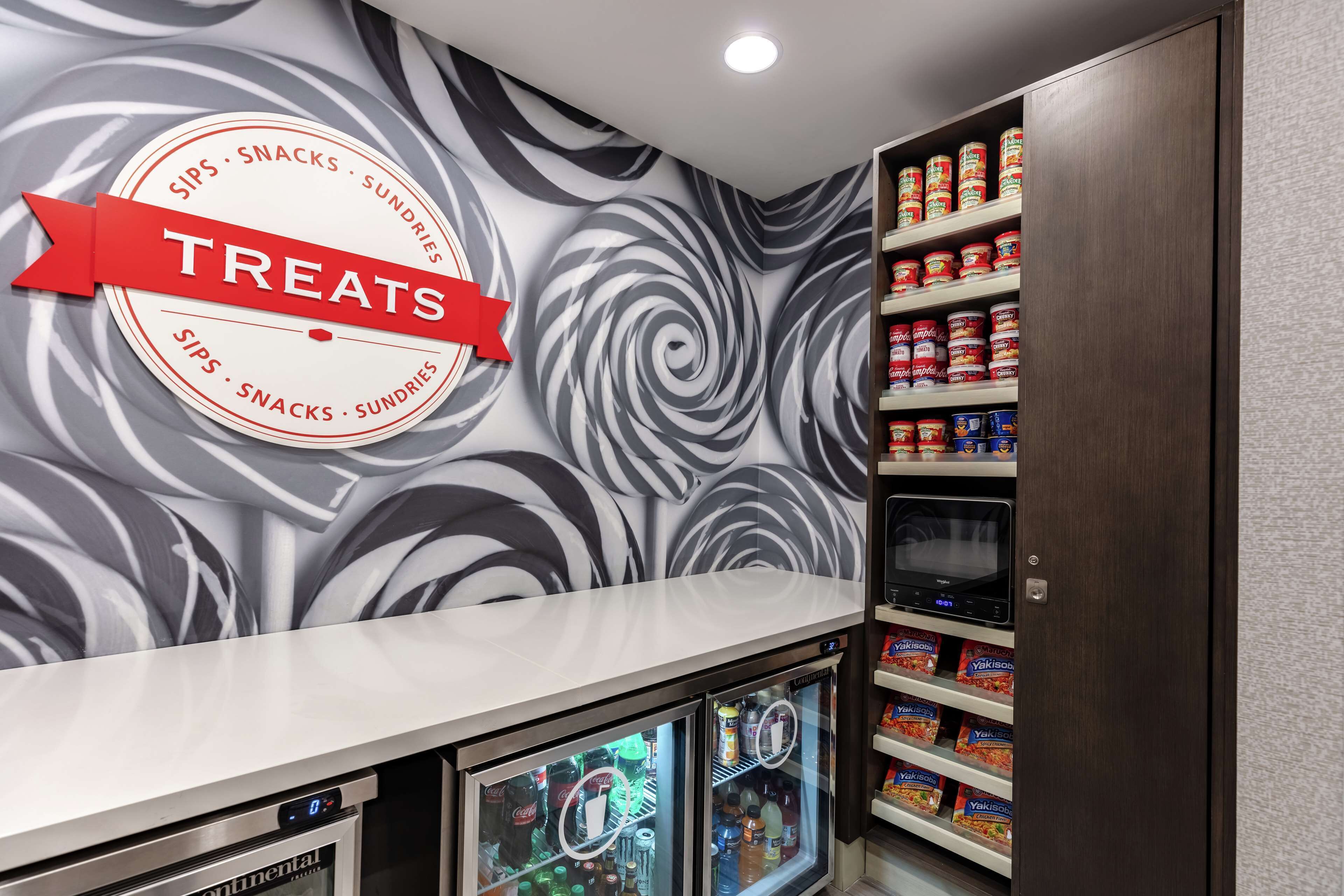 A snack bar with a 'Treats' sign, shelves stocked with snacks and drinks, and a refrigerator with beverages.