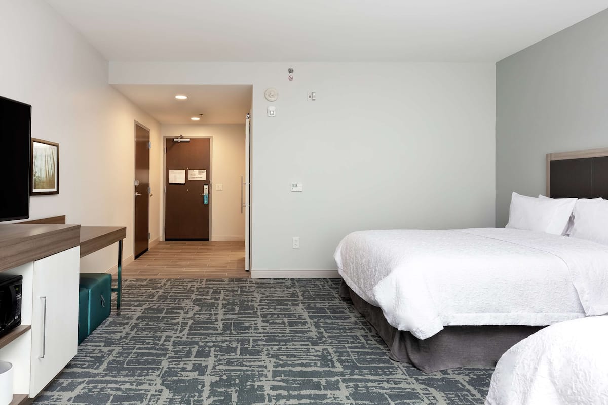 Ett hotellrum med en säng, ett skrivbord, en mikrovågsugn och en liten papperskorg.