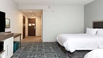 Habitación de hotel con cama, escritorio, microondas y un pequeño cubo de basura.