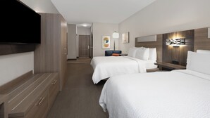 A hotel room with two beds, a flat-screen TV, a desk, and a wall-mounted light fixture.