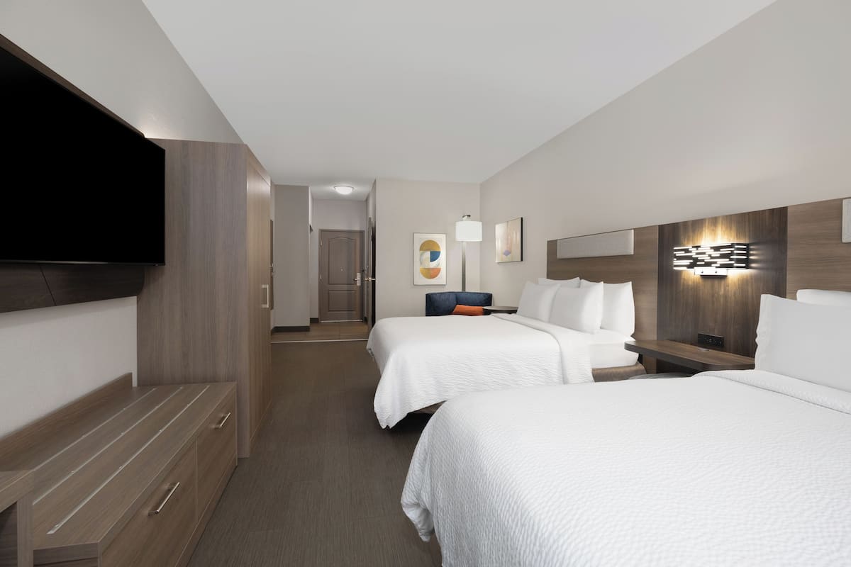 Ett hotellrum med två sängar, en platt-TV, ett skrivbord och en väggmonterad lampa.