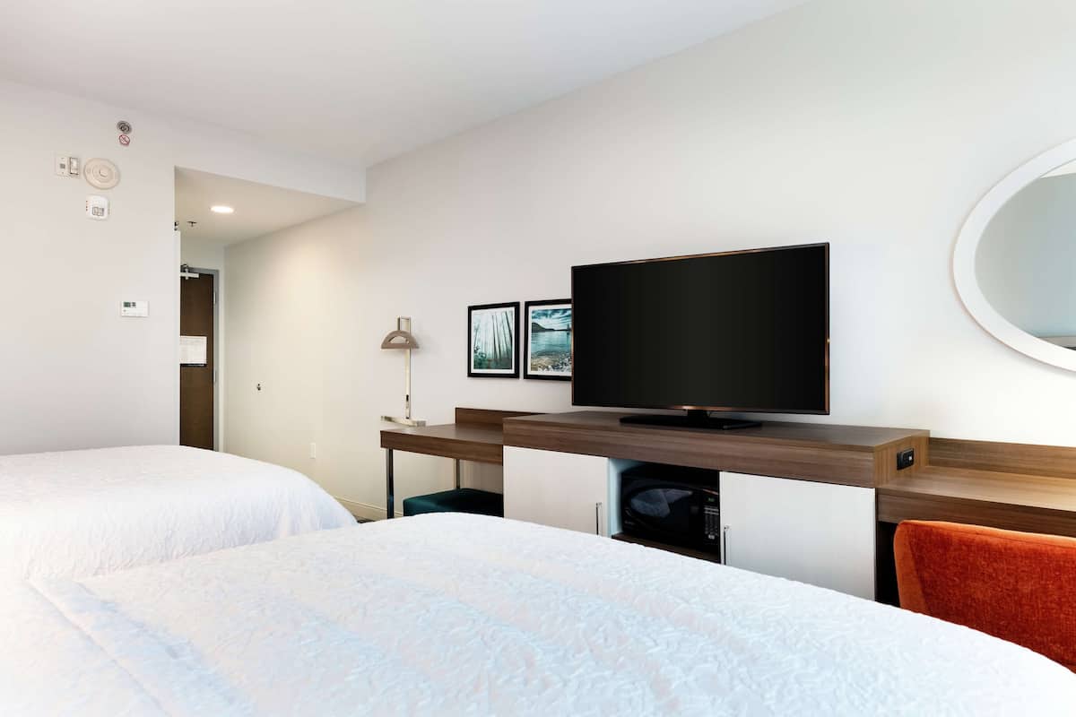 Ett hotellrum med två sängar, en TV, ett skrivbord och en spegel.