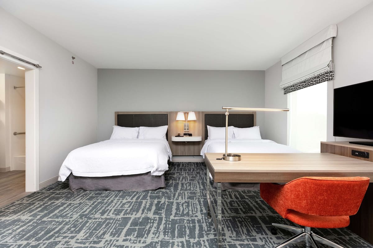 Ett hotellrum med två sängar, ett skrivbord, en stol, en TV och en lampa.