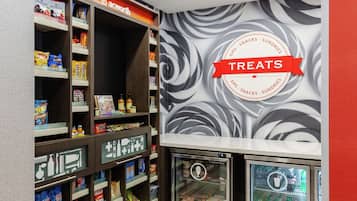 Una sección de aperitivos y artículos diversos, con estantes llenos de diferentes opciones y un refrigerador con productos frescos.