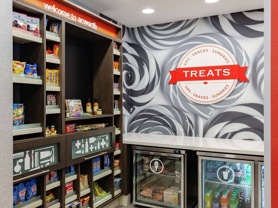 Una sección de aperitivos y artículos diversos, con estantes llenos de diferentes opciones y un refrigerador con productos frescos.