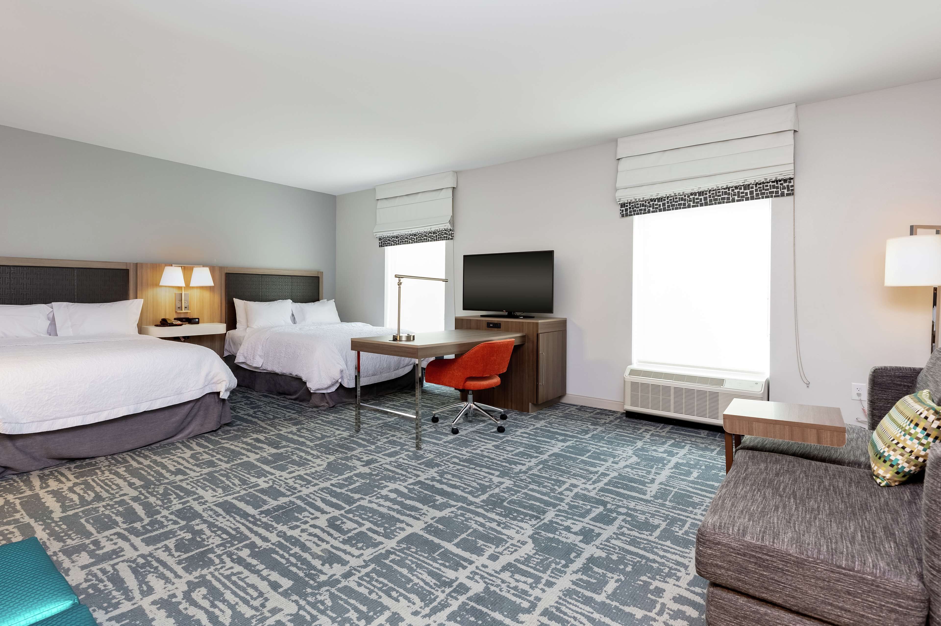 Une chambre d’hôtel avec deux lits, un bureau avec une chaise, une télévision et un canapé.