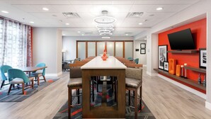 A modern hotel lobby with a long reception desk, comfortable seating, a large TV, and a decorative vase.