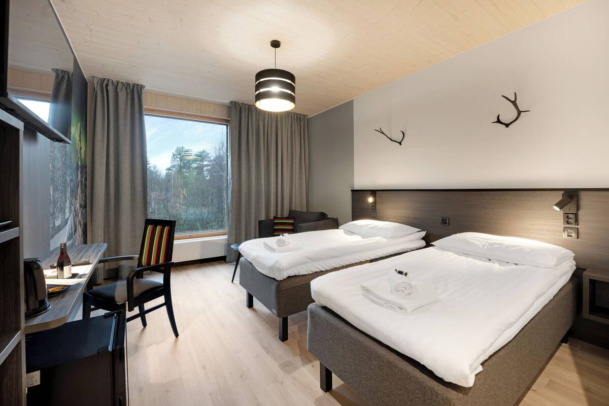 A modern hotel room with two beds, a desk, a chair, and a large window with curtains.