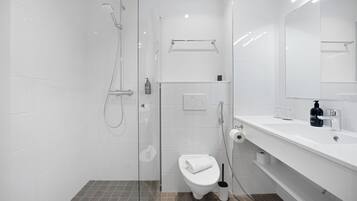 Un baño moderno con ducha envuelta en vidrio, inodoro y lavabo con espejo.