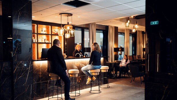 Un área de bar moderna con paredes de mármol, taburetes y lámparas colgantes.