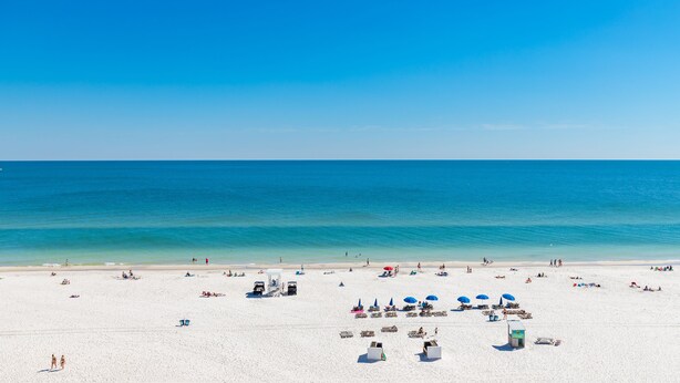 A beach with white sand, clear blue water, and umbrellas. - Phoenix All Suites (Gulf Shores)