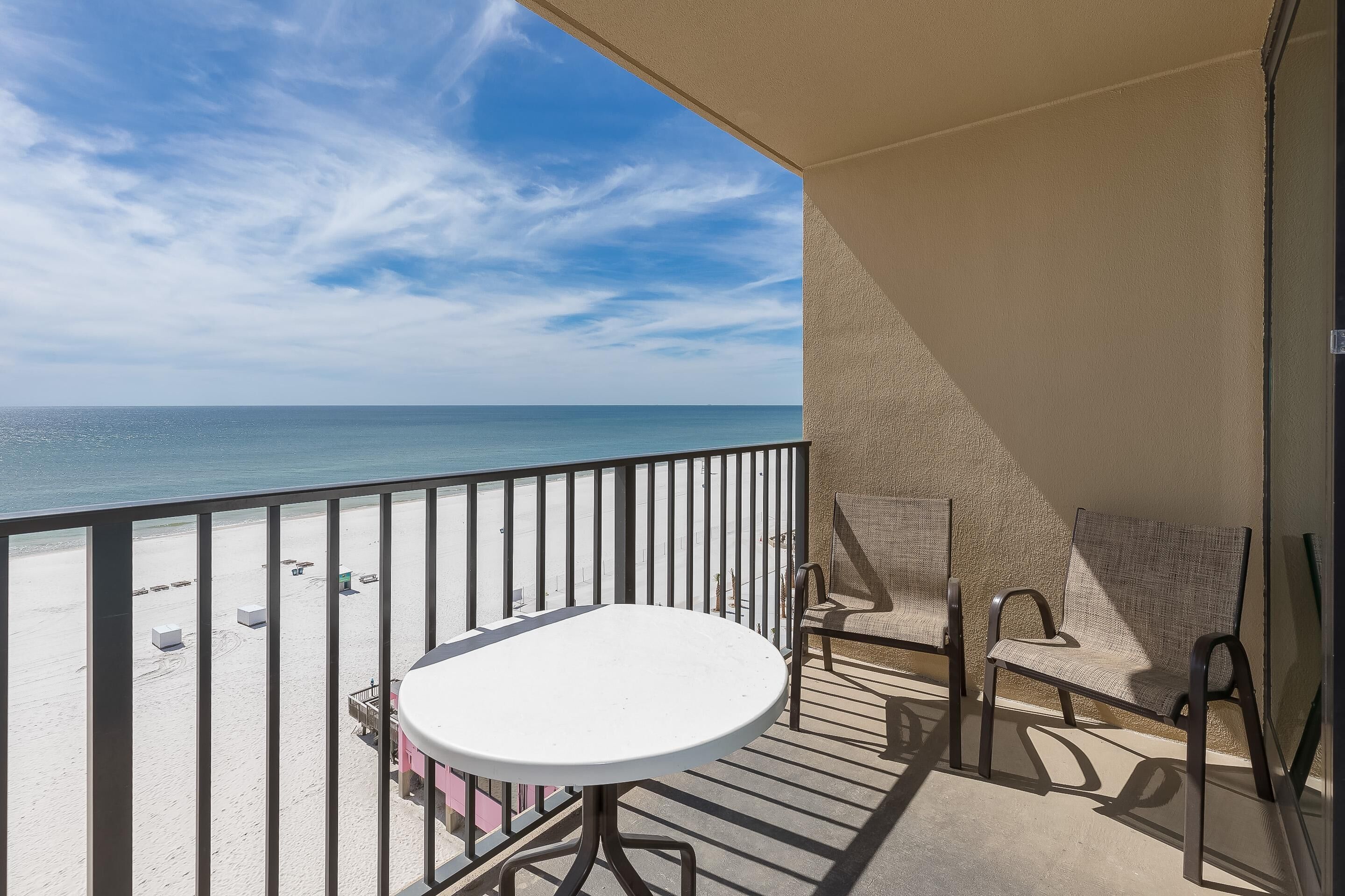 Un balcone con tavolo e due sedie, vista su una spiaggia, l'oceano e un cielo sereno.