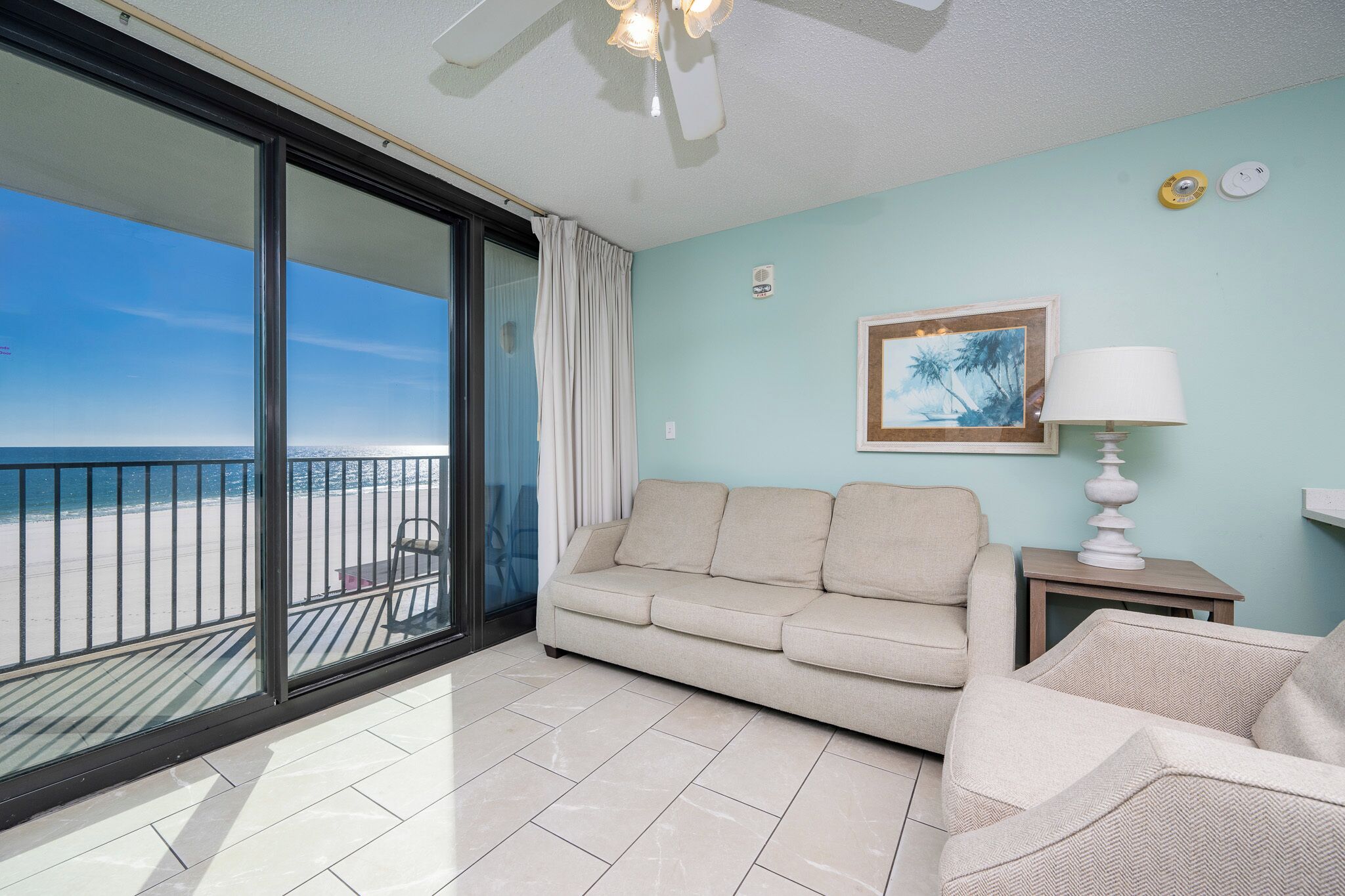 Een balkon met uitzicht op het strand, een bank, een stoel en een lamp.