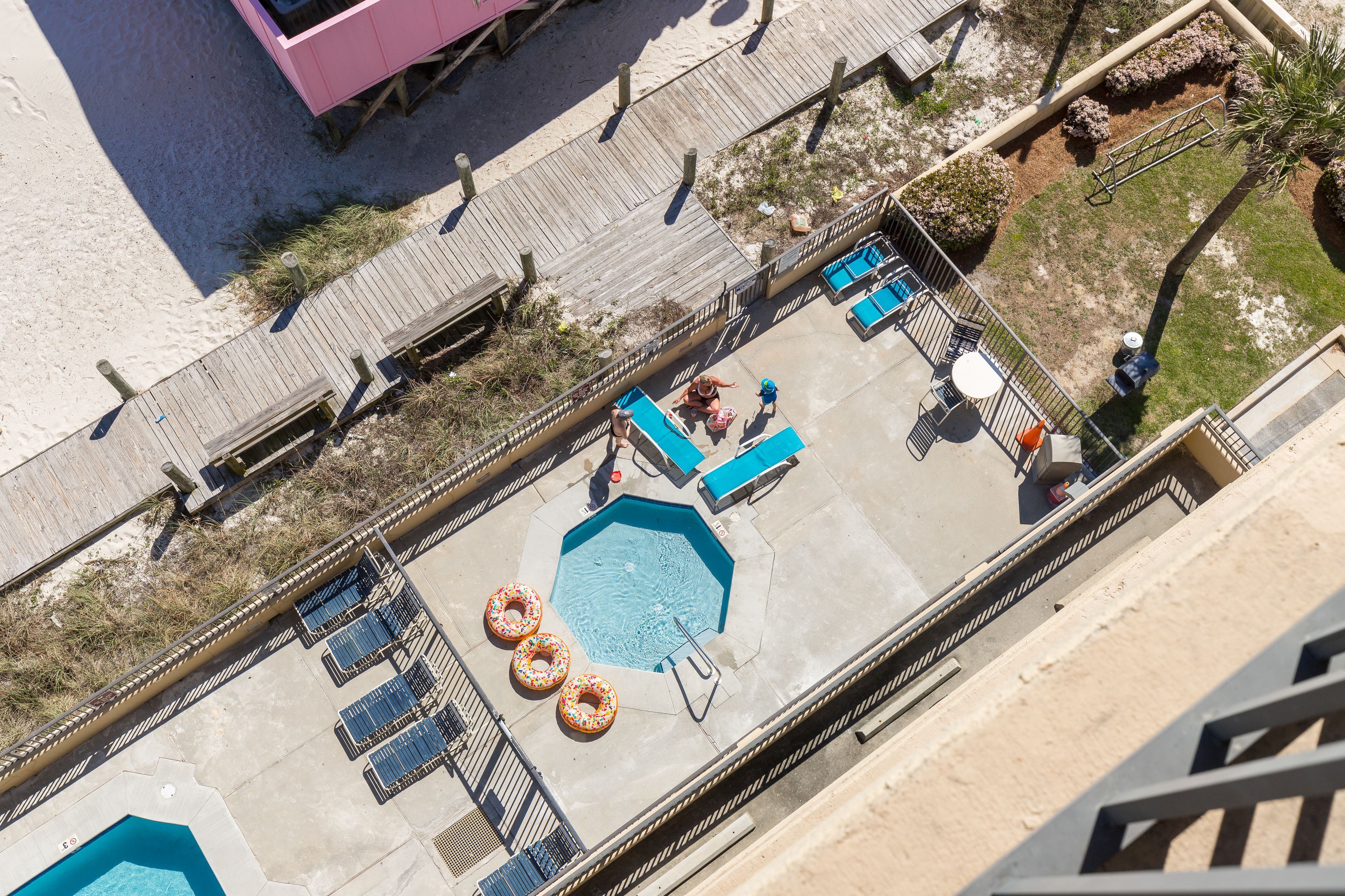 An aerial view of a rooftop pool area with a hexagonal pool, lounge chairs, and a wooden deck.