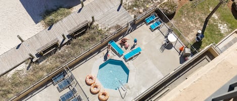 An aerial view of a rooftop pool area with a hexagonal pool, lounge chairs, and a wooden deck.