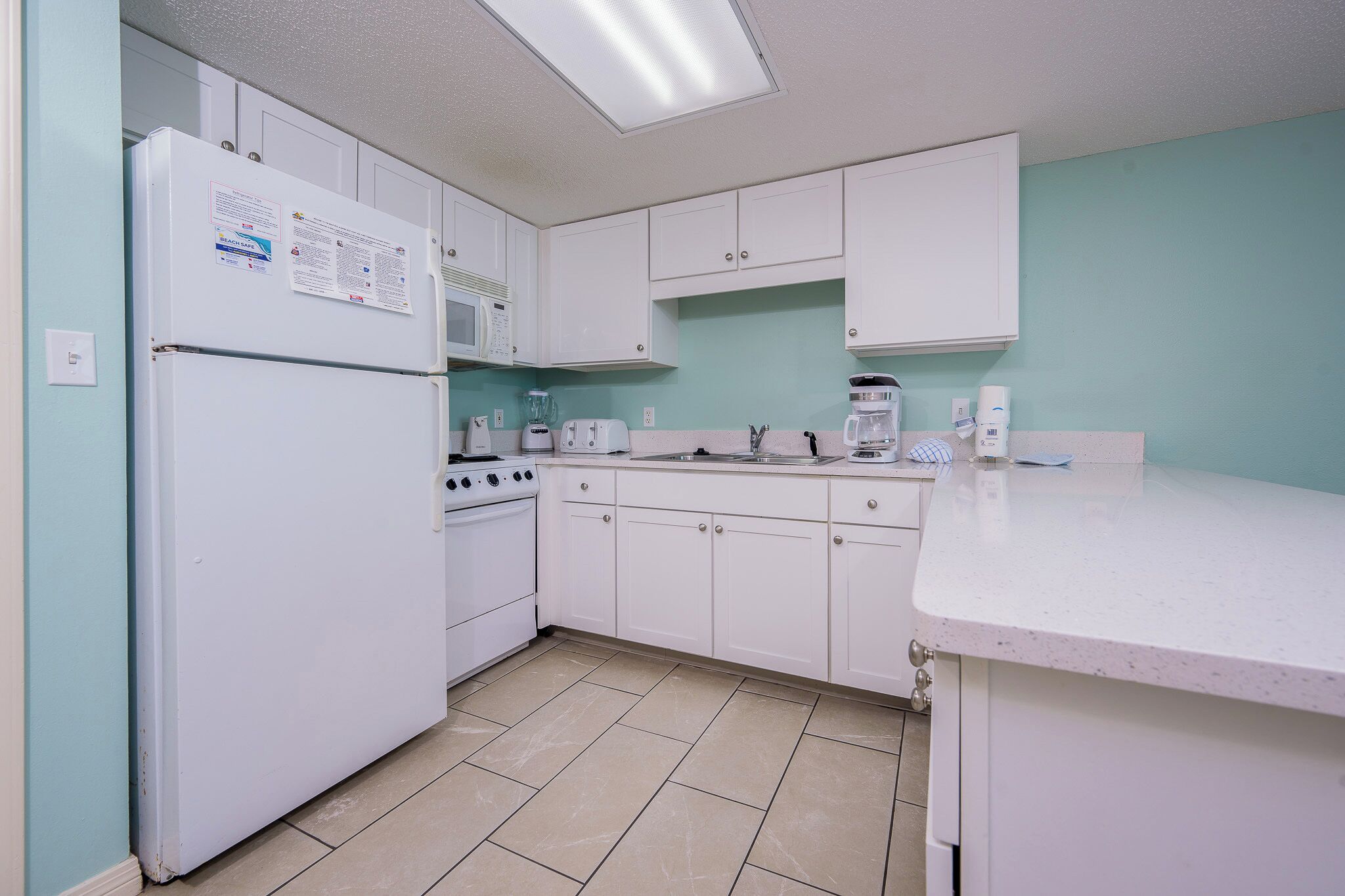 Una cocina con gabinetes blancos, un refrigerador, un microondas, una estufa y un lavamanos.