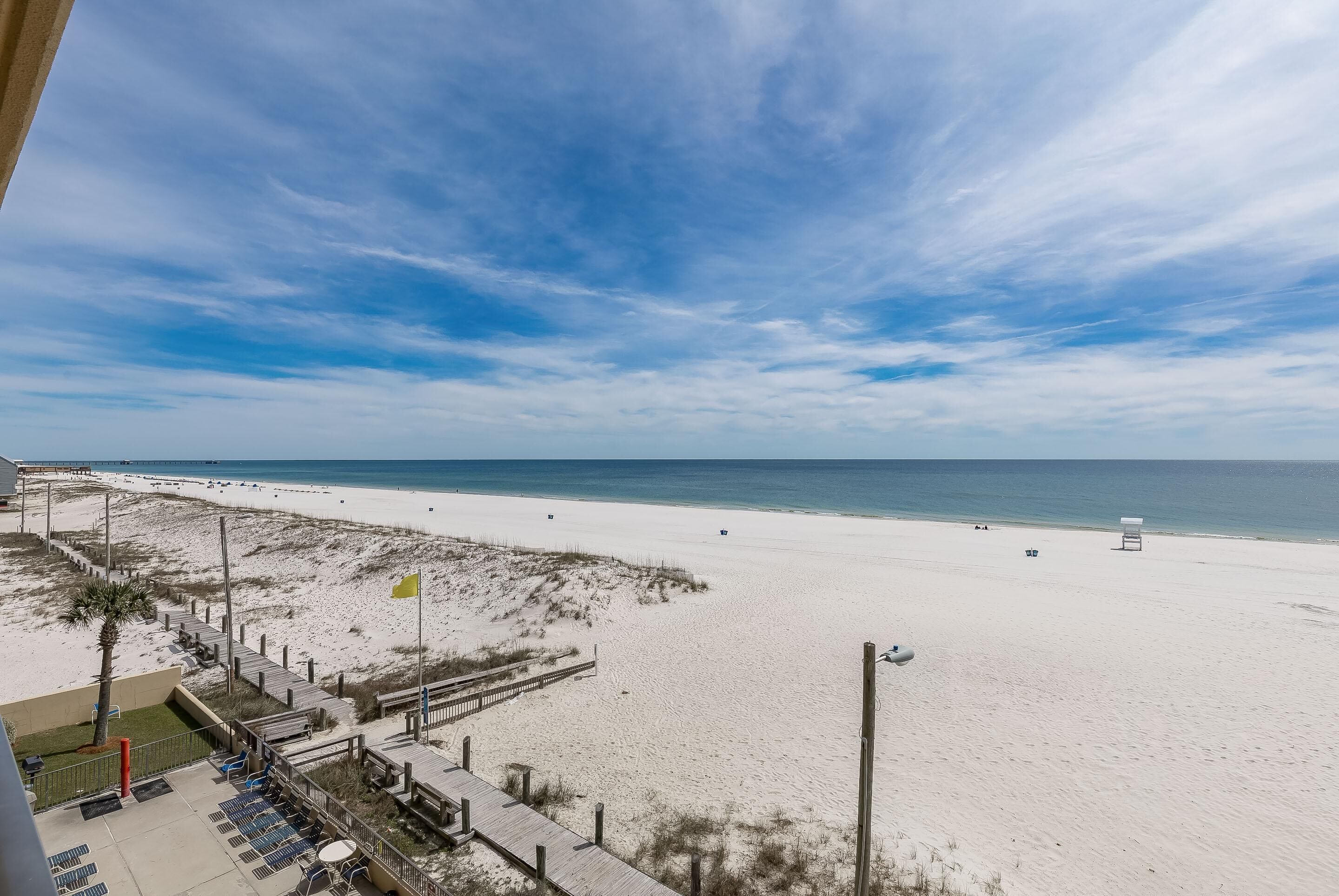 Blick auf einen Strand vom Hotelbalkon, mit Sandstrand, Meer und einer Holzpromenade.