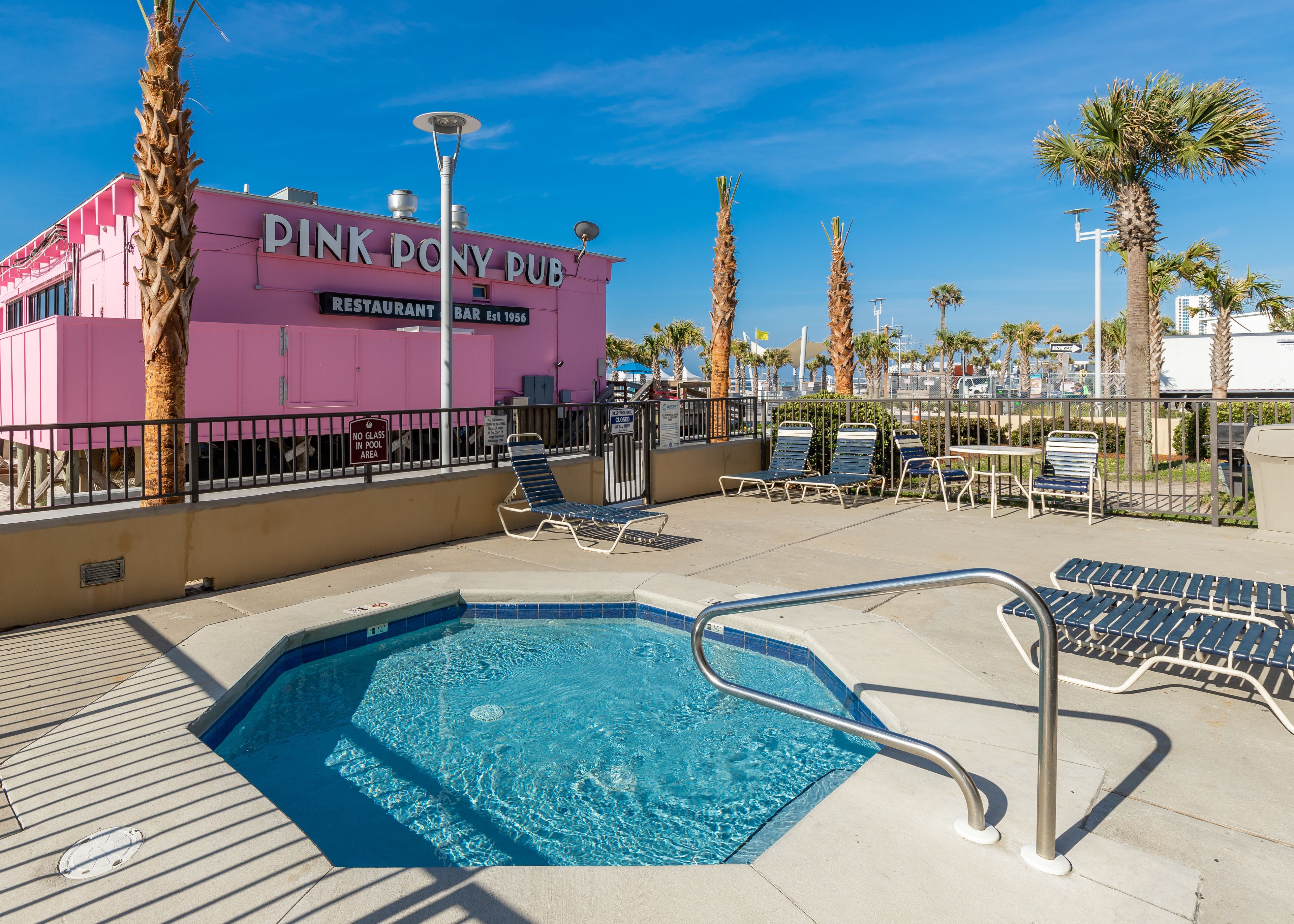 A pool area with lounge chairs, a pink building labeled "PINK PONY PUB," and palm trees.