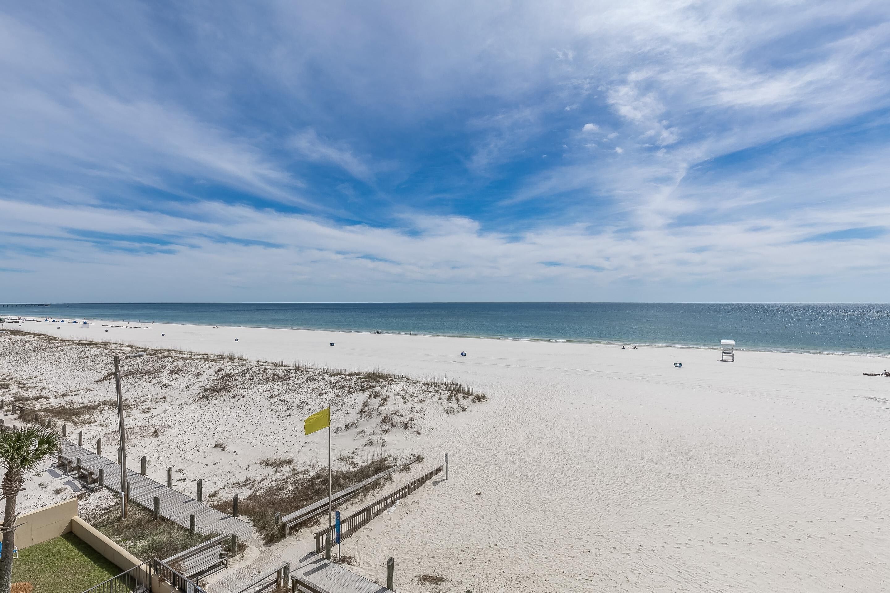 A beach with a wooden boardwalk, a flag, and a clear sky.