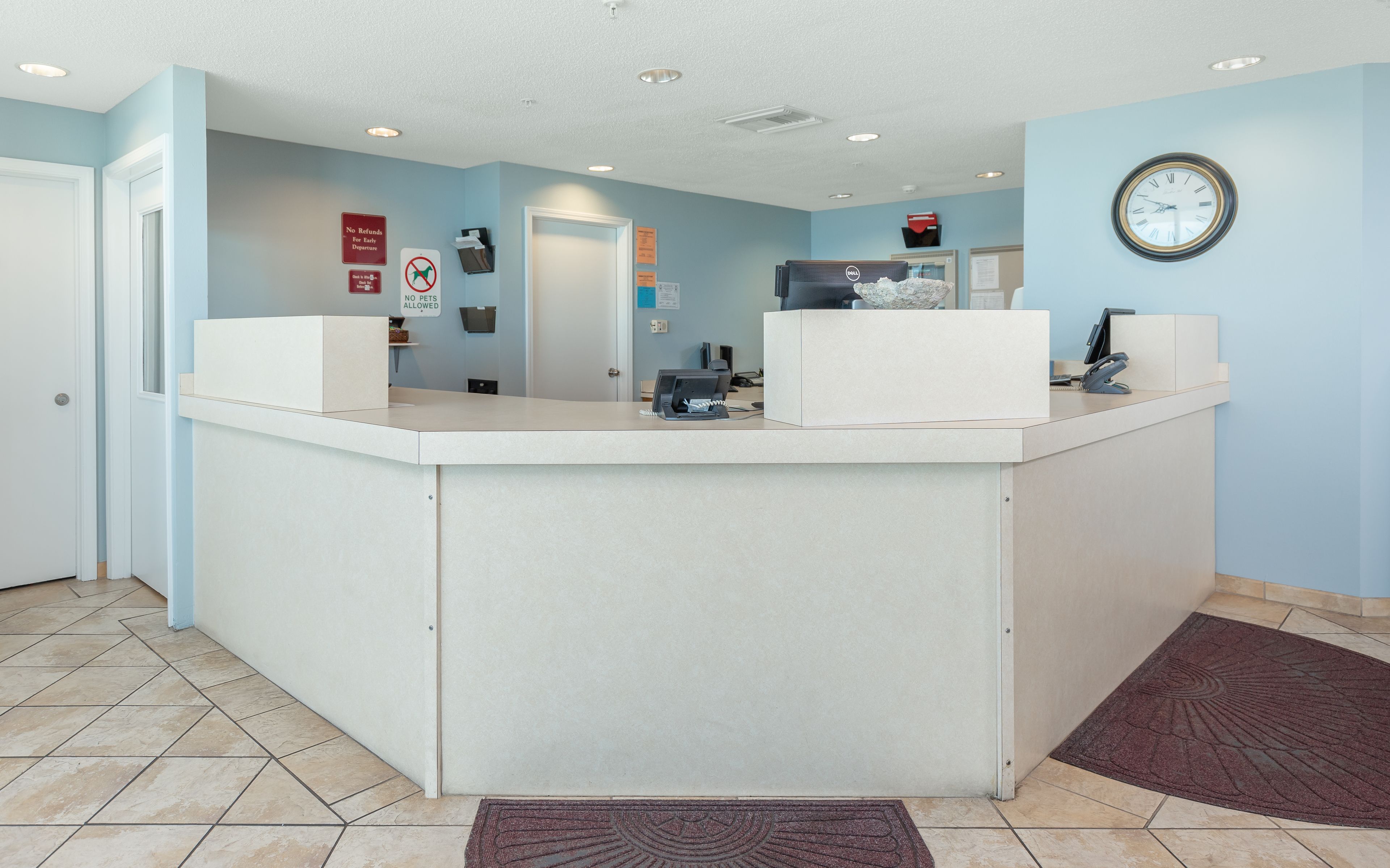 A reception area with a white reception desk, a clock on the wall, and a no pets allowed sign.