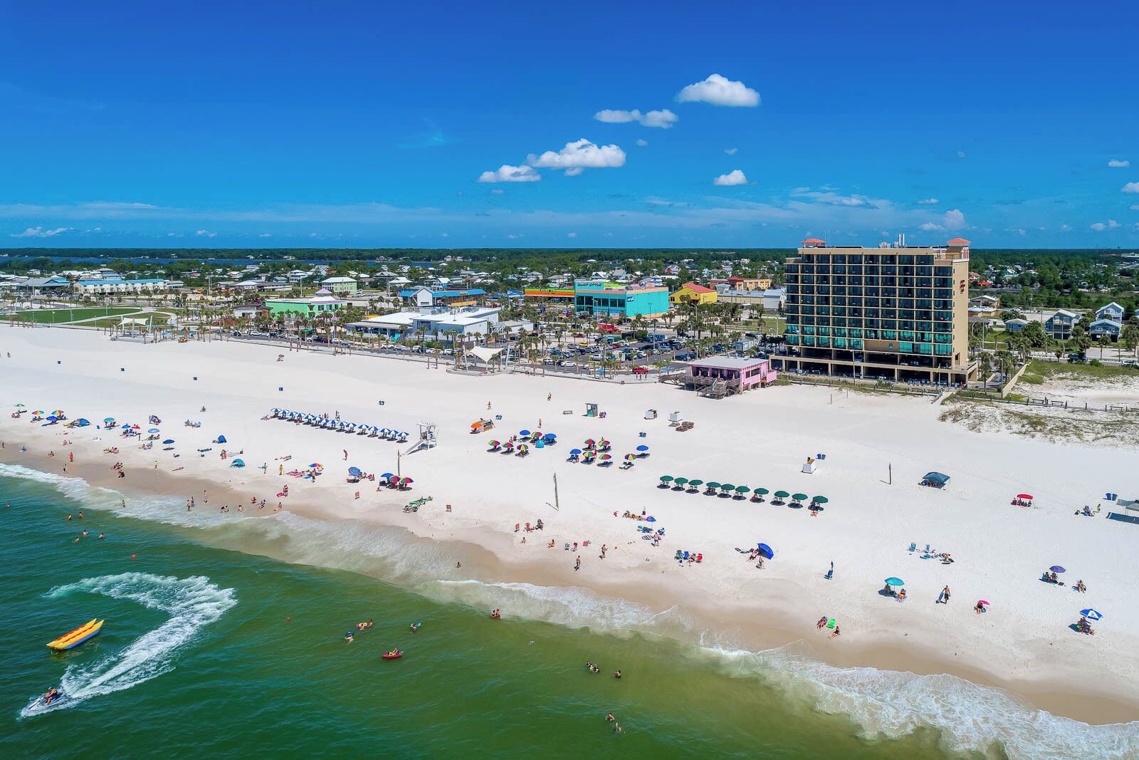 A beach resort with a large building, numerous beach umbrellas, and a clear view of the ocean.