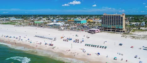 A beach resort with a large building, numerous beach umbrellas, and a clear view of the ocean.