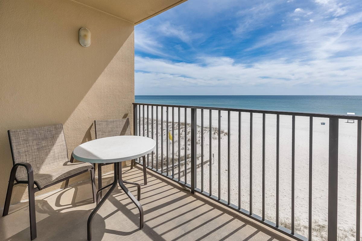Un balcon avec une table et des chaises, donnant sur une plage et muni d’une rambarde.