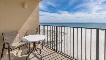 A balcony with a table and chairs, overlooking a beach with a railing.