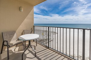 A balcony with a table and chairs, overlooking a beach with a railing.