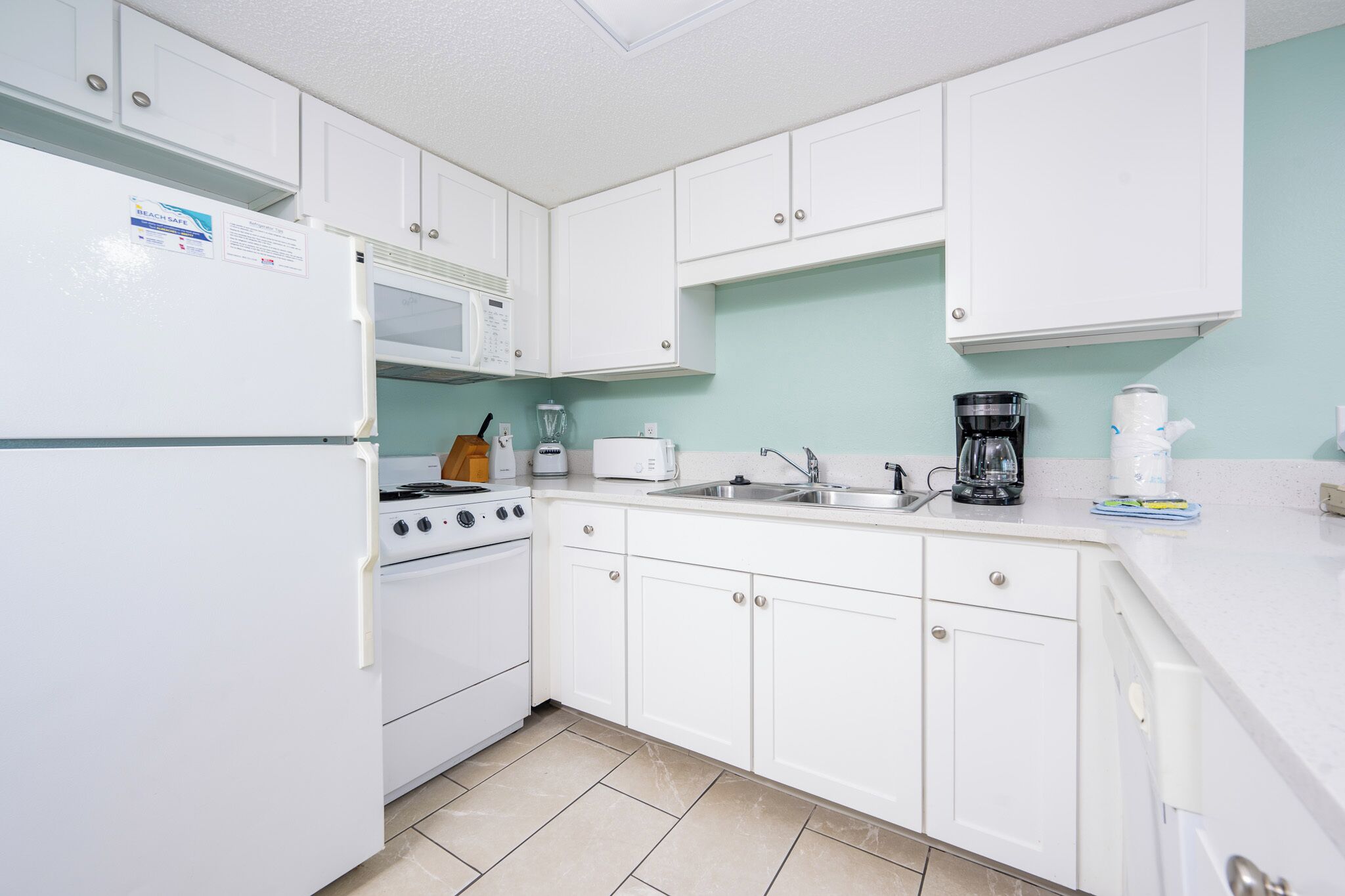 A kitchen with white cabinets, a stove, a microwave, a coffee maker, and a toaster.