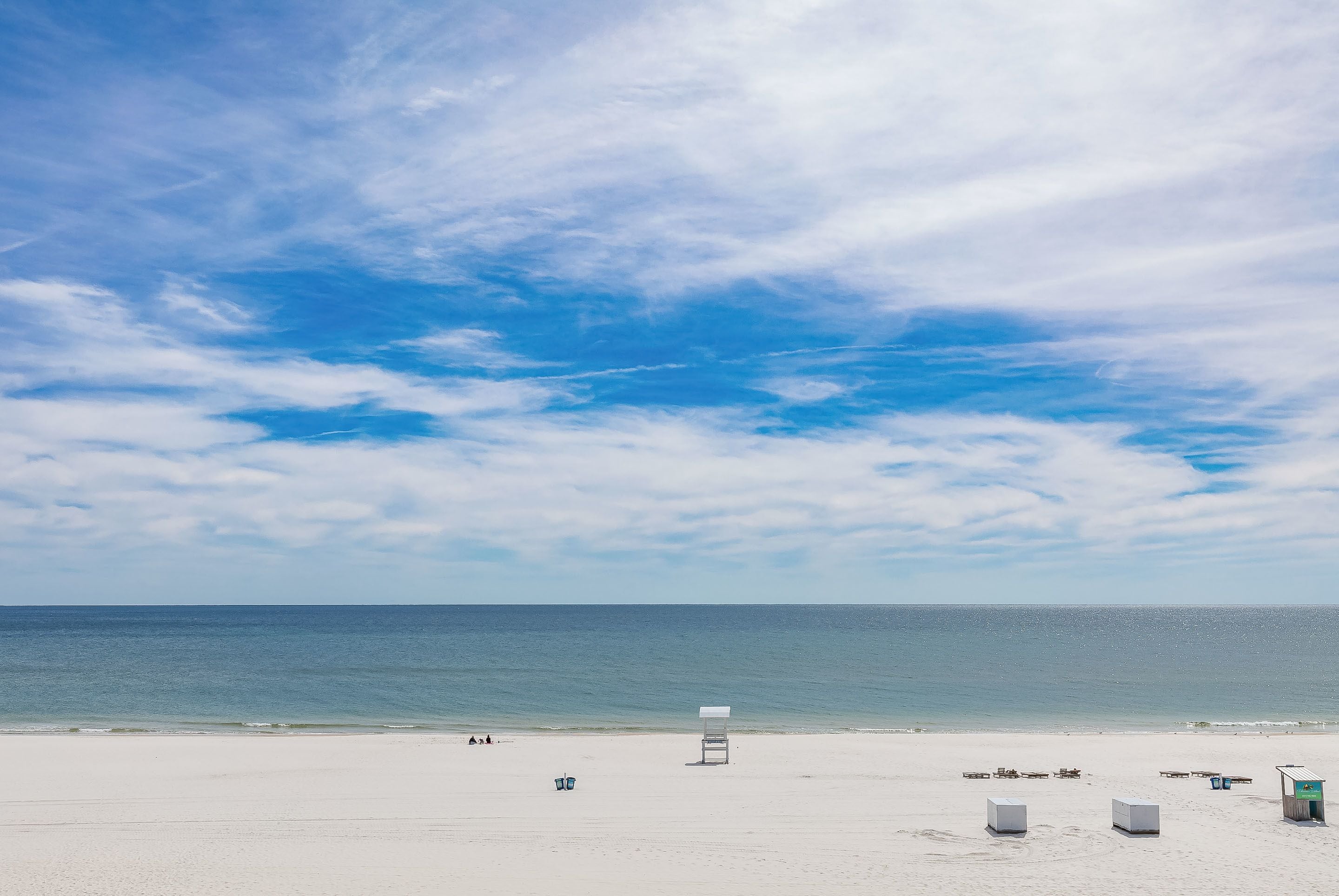 A beach with a lifeguard tower, a few beach chairs, and a small structure, likely a restroom or storage.
