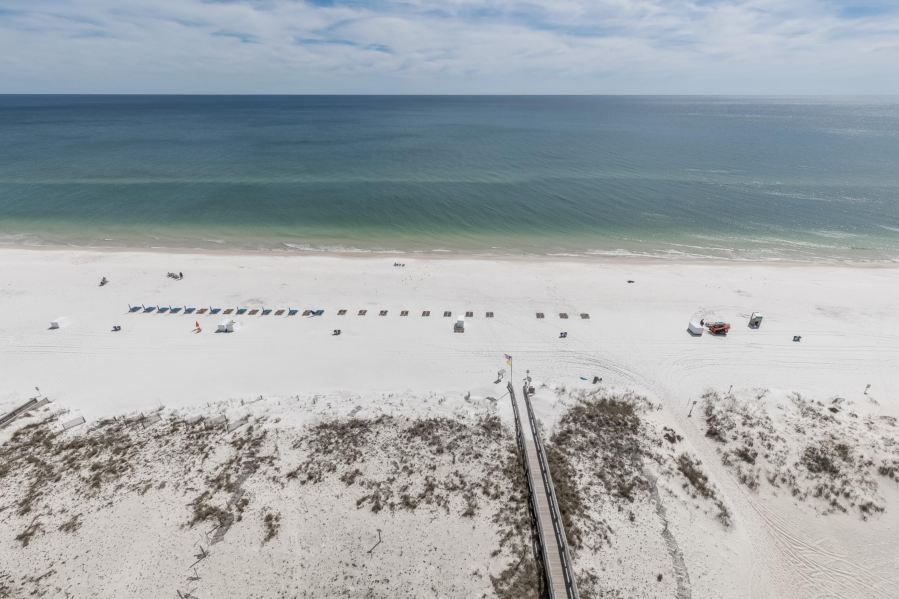A beach with a long pier extending into the ocean, a row of beach umbrellas, and a few beach chairs.
