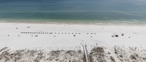 A beach with a long pier extending into the ocean, a row of beach umbrellas, and a few beach chairs.