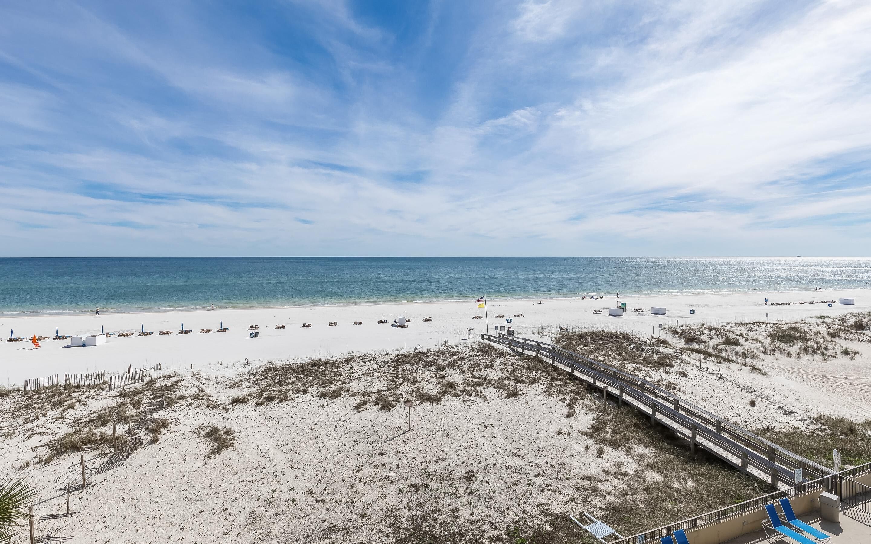 A beach with a wooden boardwalk, sandy dunes, and a clear view of the ocean.