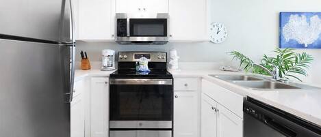 A modern kitchen with stainless steel appliances, white cabinetry, a built-in oven, a microwave, and a sink.