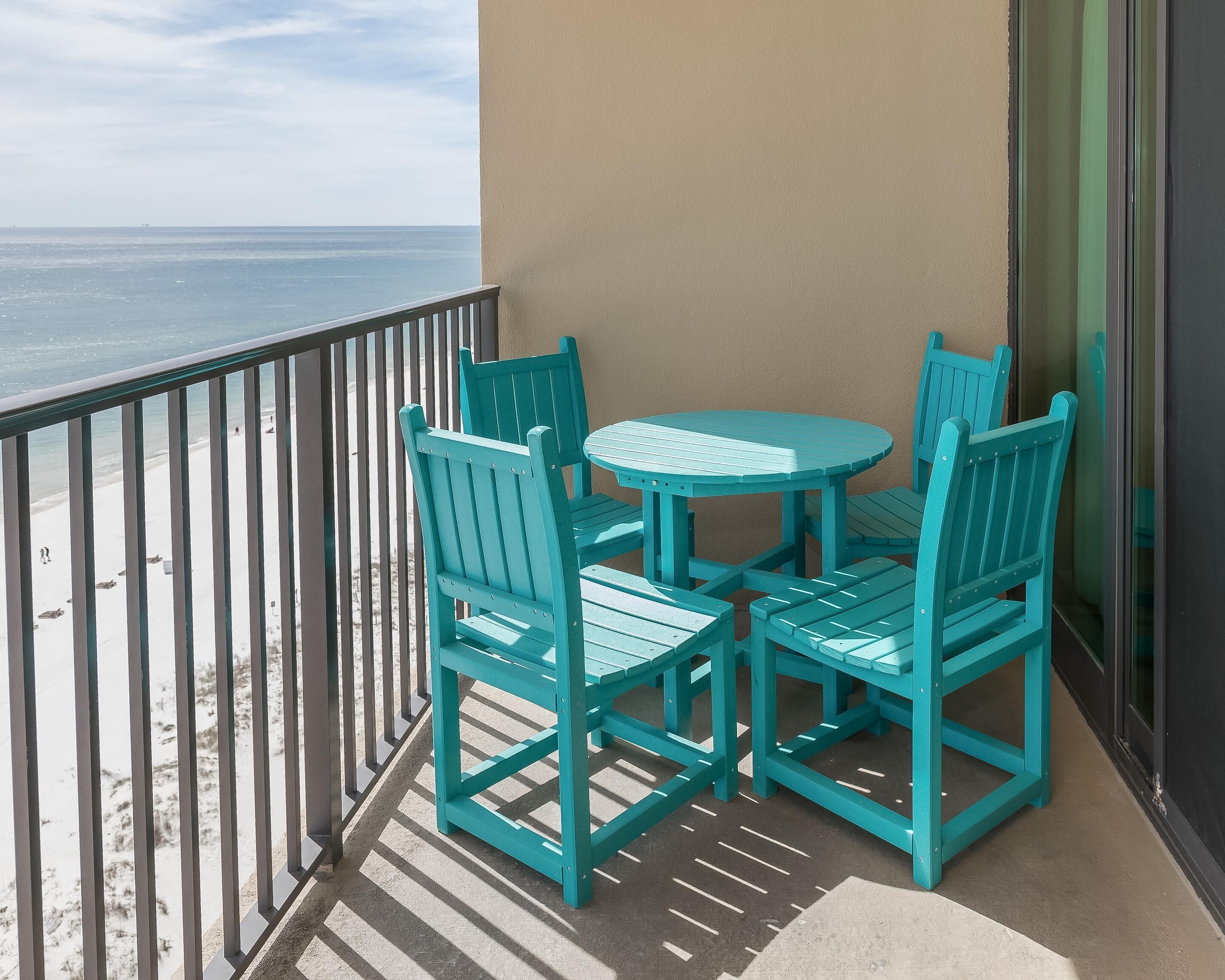 A balcony with a turquoise table and chairs, overlooking a beach.