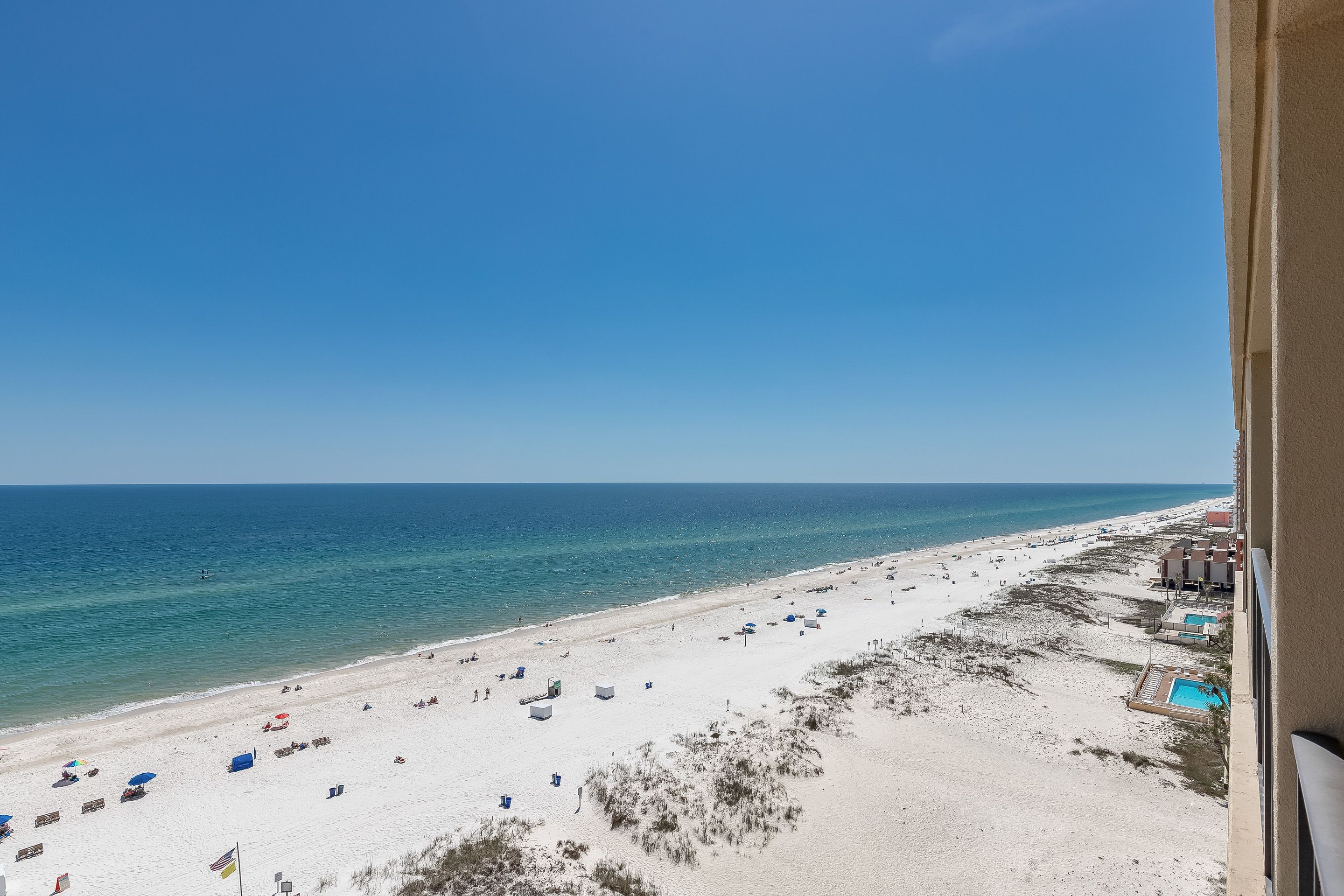 Uitzicht op een strand vanaf een balkon, met heldere lucht, zandstrand en een zwembad.