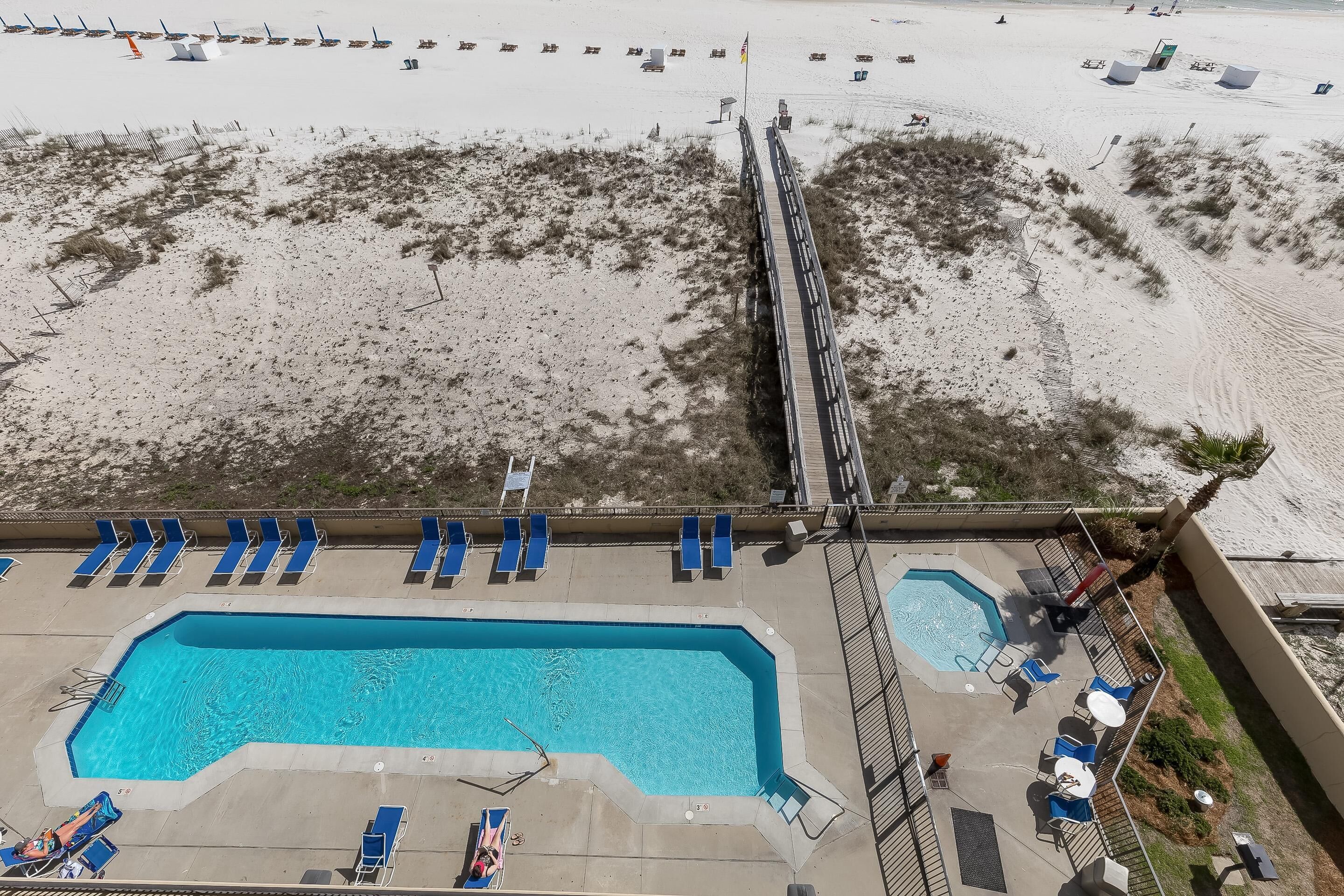 Una piscina con agua azul, rodeada de sillas reclinables azules y una zona de terraza.