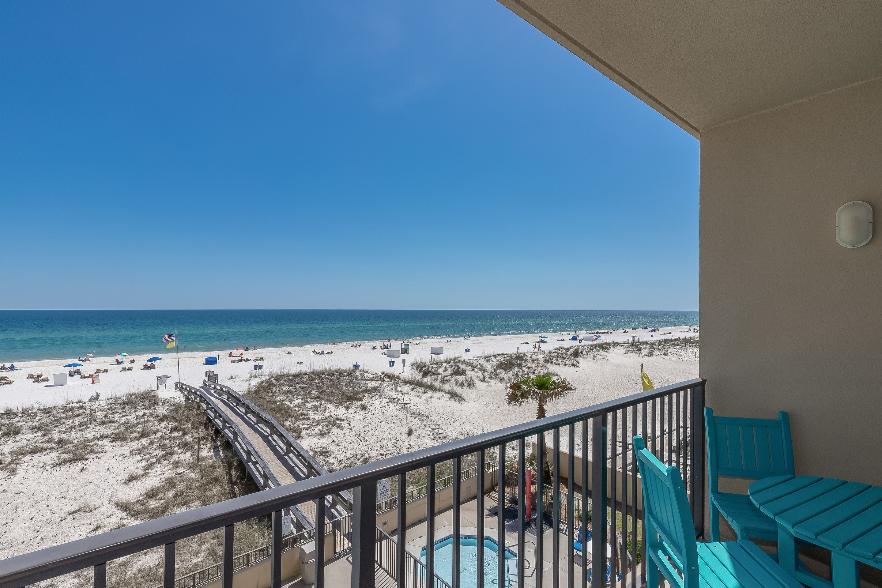 A balcony with a pool, beach view, and turquoise chairs.